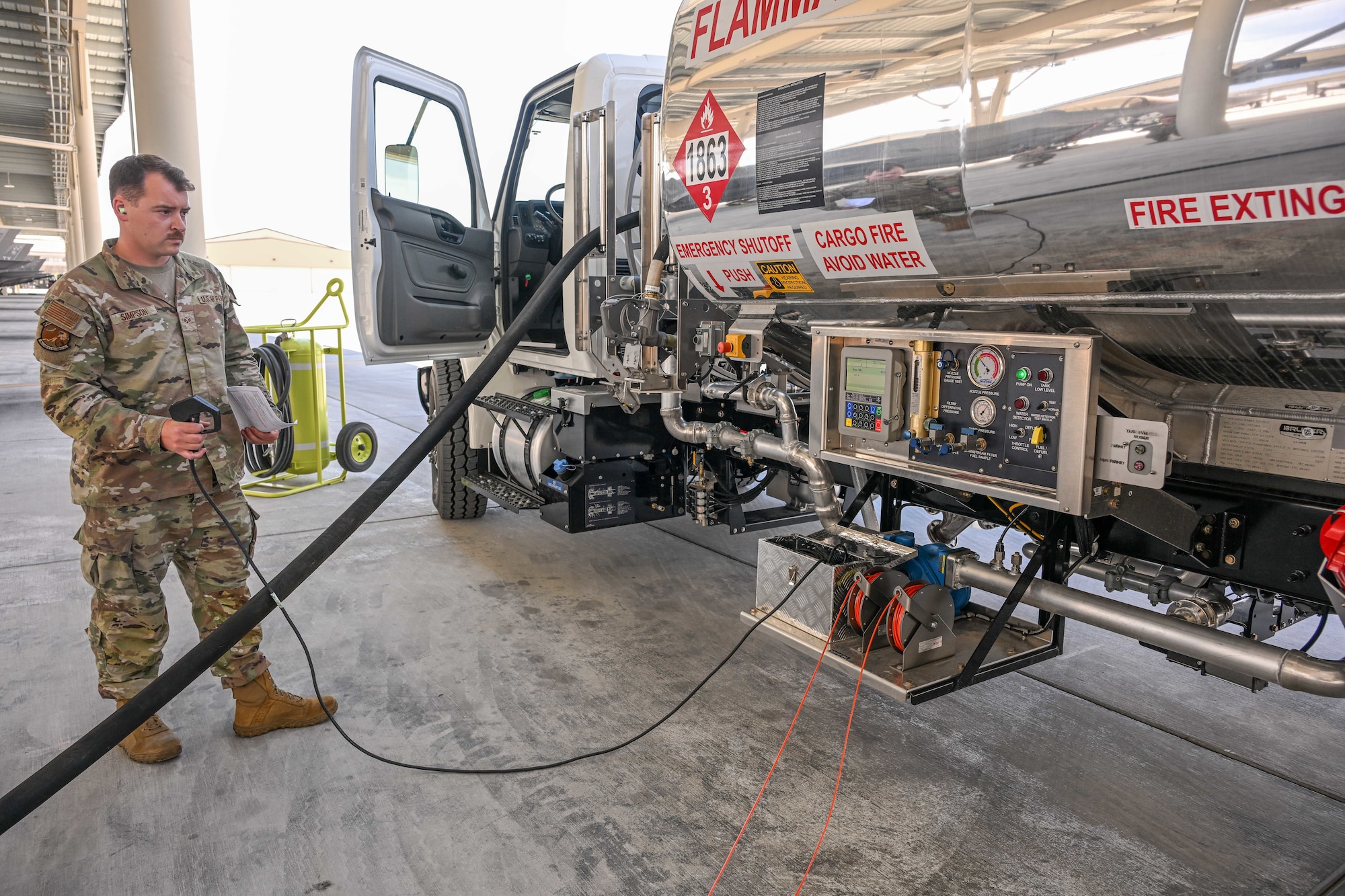 Military airman operating a fuel hose connected to a large fuel tanker on a flightline