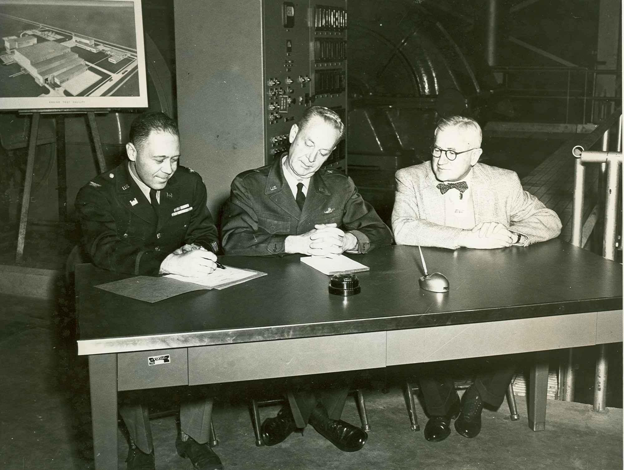 Col. L.E. Cox, engineer with the Tullahoma District of the U.S. Army Corps of Engineers, left, prepares to turn the Arnold Engineering Development Center Engine Test Facility Exhaust Compressor Building over to then-AEDC Commander Brig. Gen. Samuel Harris, center, during a Nov. 30, 1953, ceremony at the Center. Harris then indorsed the building and equipment over to Thomas Farrell, managing director of Arnold Research Organization, right. ARO was the corporation established to maintain and operate AEDC. In the background is one of the six compressors contained within the Exhaust Compressor Building which, up to that point, was the largest single unit completed at AEDC. (U.S. Air Force photo)