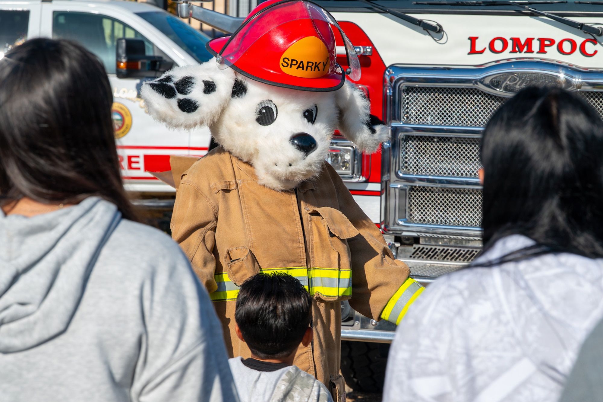 A puppy mascot motions to hug a community member