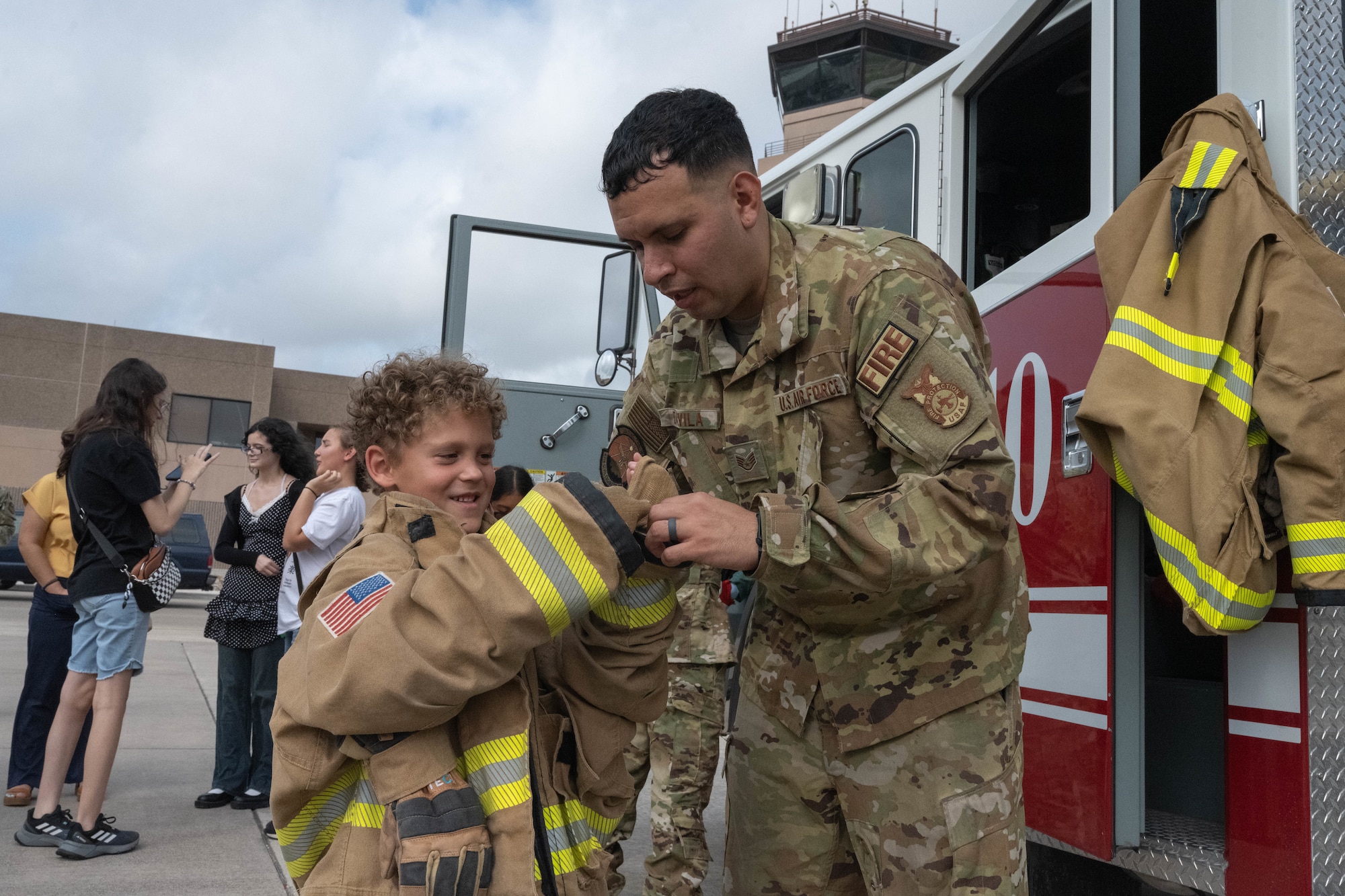 A participant of Tiger for a Day receives assistance from U.S. Air Force Staff Sgt. Oscar Davila, 47th Civil Engineering Squadron (CES) lead fire fighter, while trying on a fire fighter suit at Laughlin Air Force Base, Texas, August 5, 2026. Fire fighters assigned to the 47 CES educated Tiger for a Day participants about their daily operations and equipment. (U.S. Air Force photo by Airman 1st Class Darryl Keith)