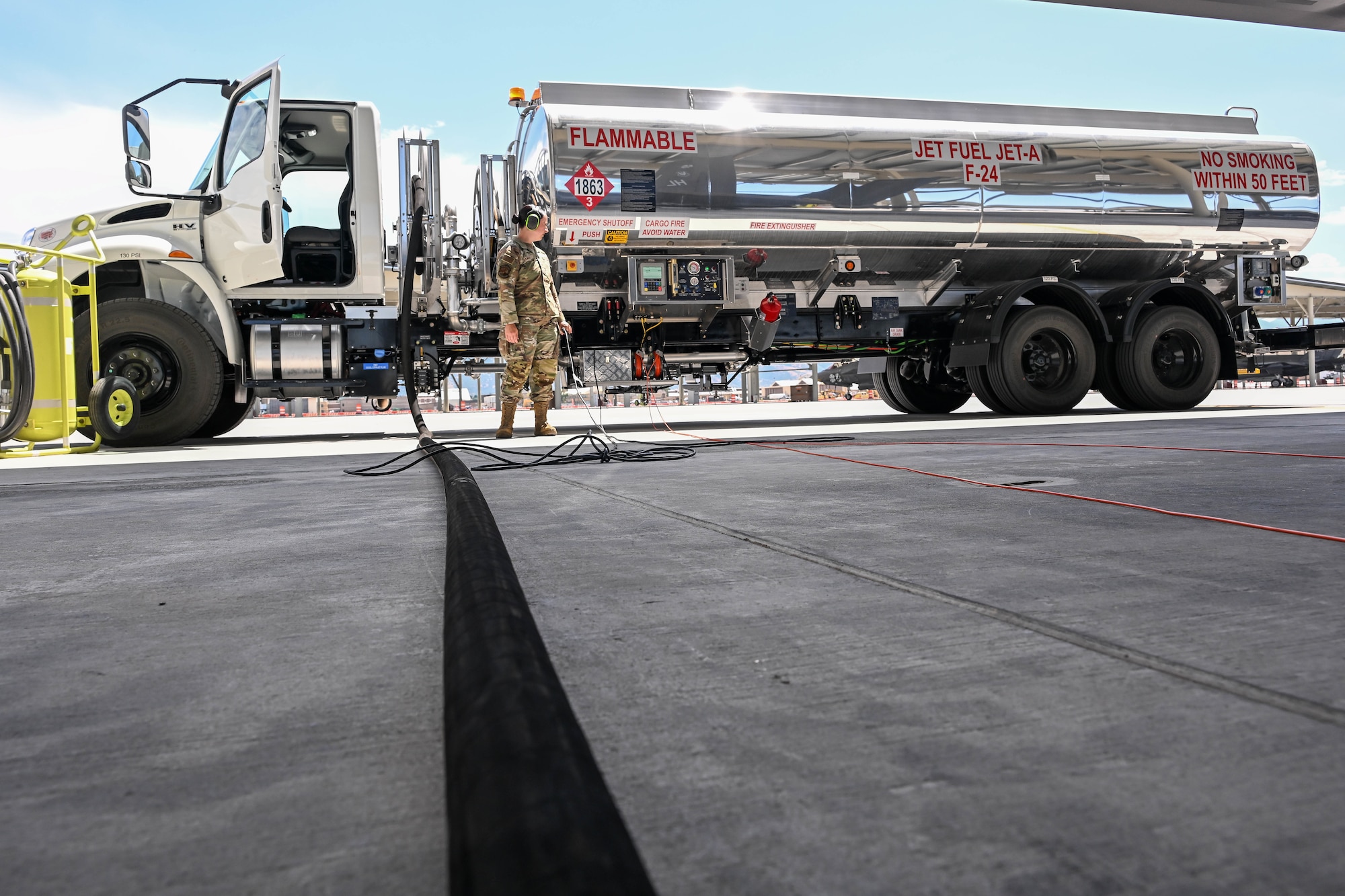 Military female airman monitoring a large fuel tanker truck refueling on an airfield.
