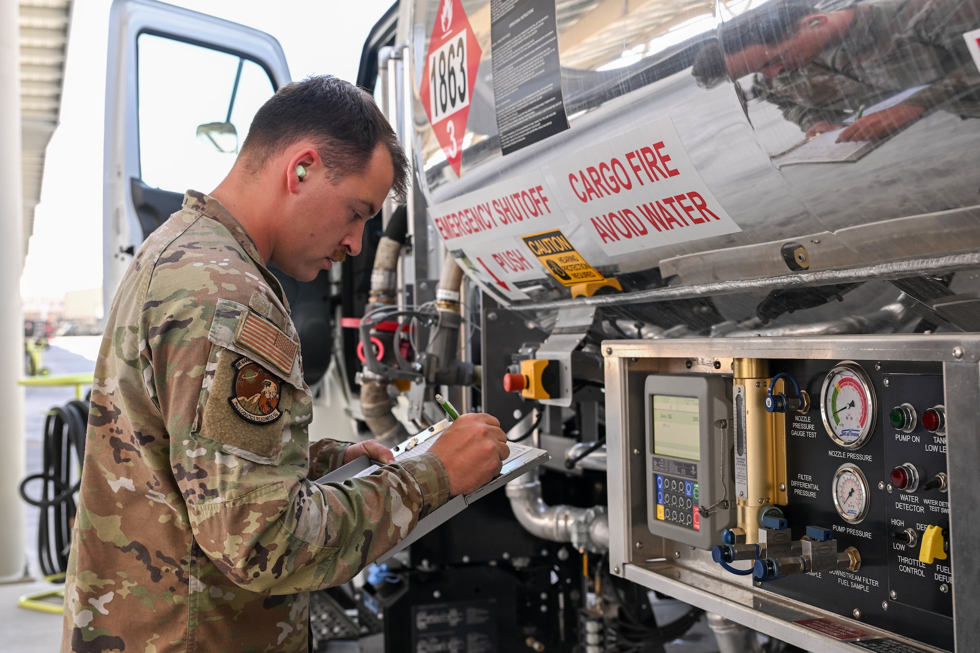 Military Airman in camoflauge inspecting and recording data from a fuel tanker control panel