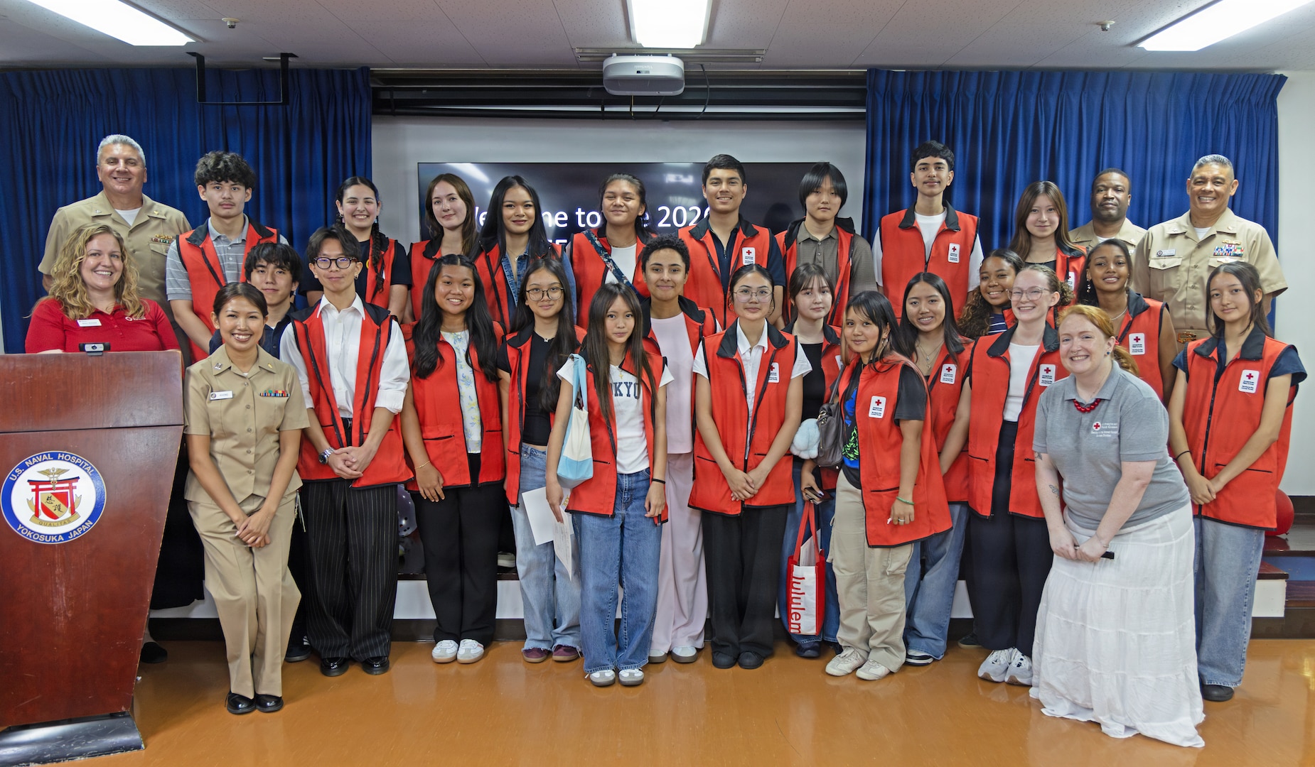 YOKOSUKA, Japan (July 31, 2026) – Capt. Joshua Miller, commanding officer of U.S. Navy Medicine Readiness and Training Command (USNMRTC) Yokosuka and director of U.S. Naval Hospital (USNH) Yokosuka, and American Red Cross staff pose for a group photo with the summer VolunTEEN participants at USNH Yokosuka. Twenty-six military-affiliated teens completed the six-week program, which provides hands-on professional development and gives participants insight into military healthcare by allowing them to shadow providers in 12 different hospital departments. (U.S. Navy photo by Ai Hazama, USNMRTC Yokosuka Public Affairs)