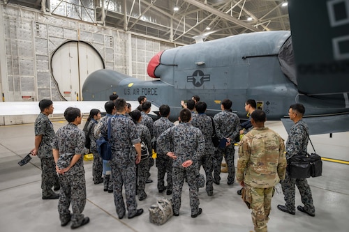 U.S. and Japanese Airman look at a drone in a hangar.
