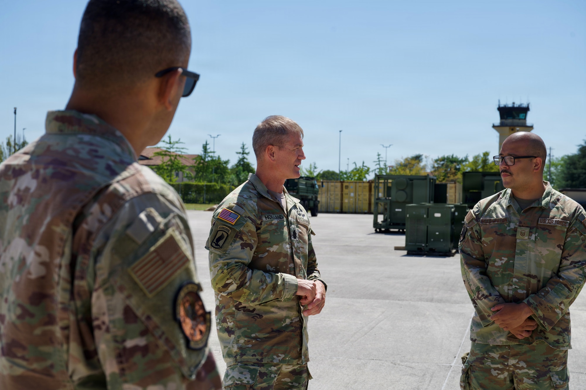 Three soldiers stand and have a conversation outside.