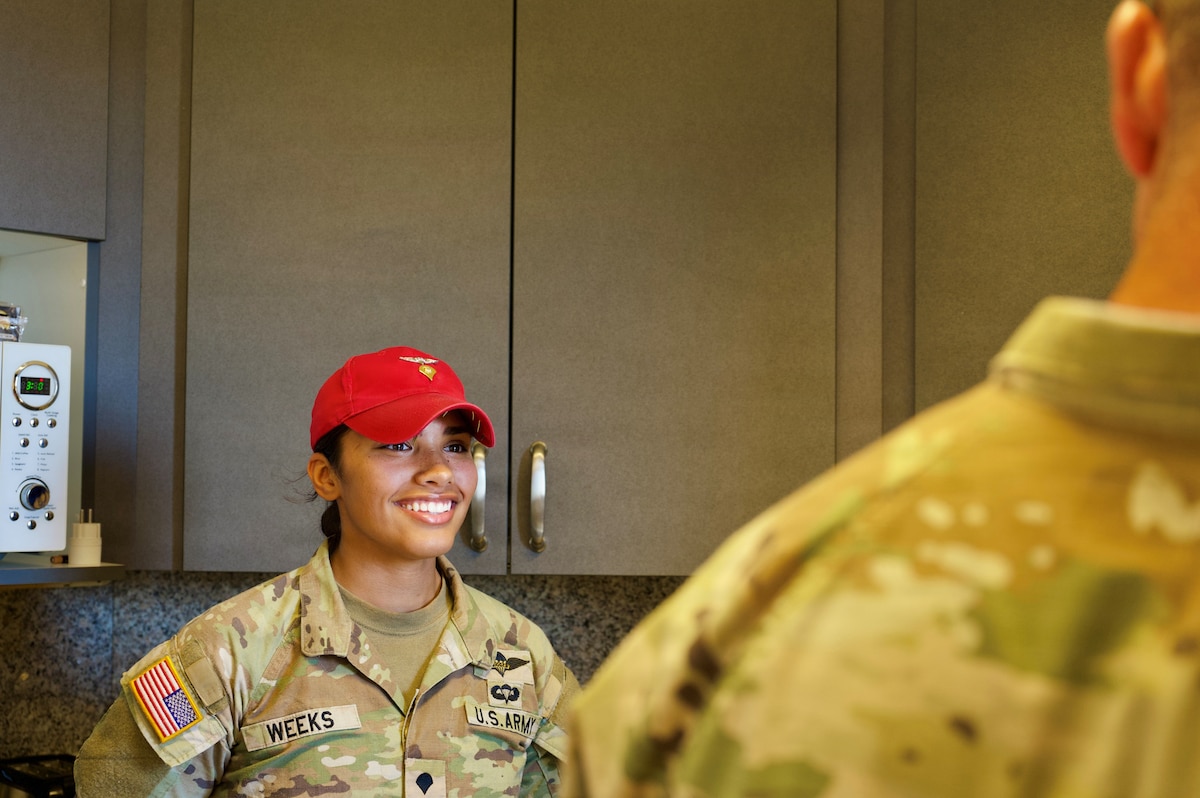 Female soldier in a red hat, smiles at another soldier.