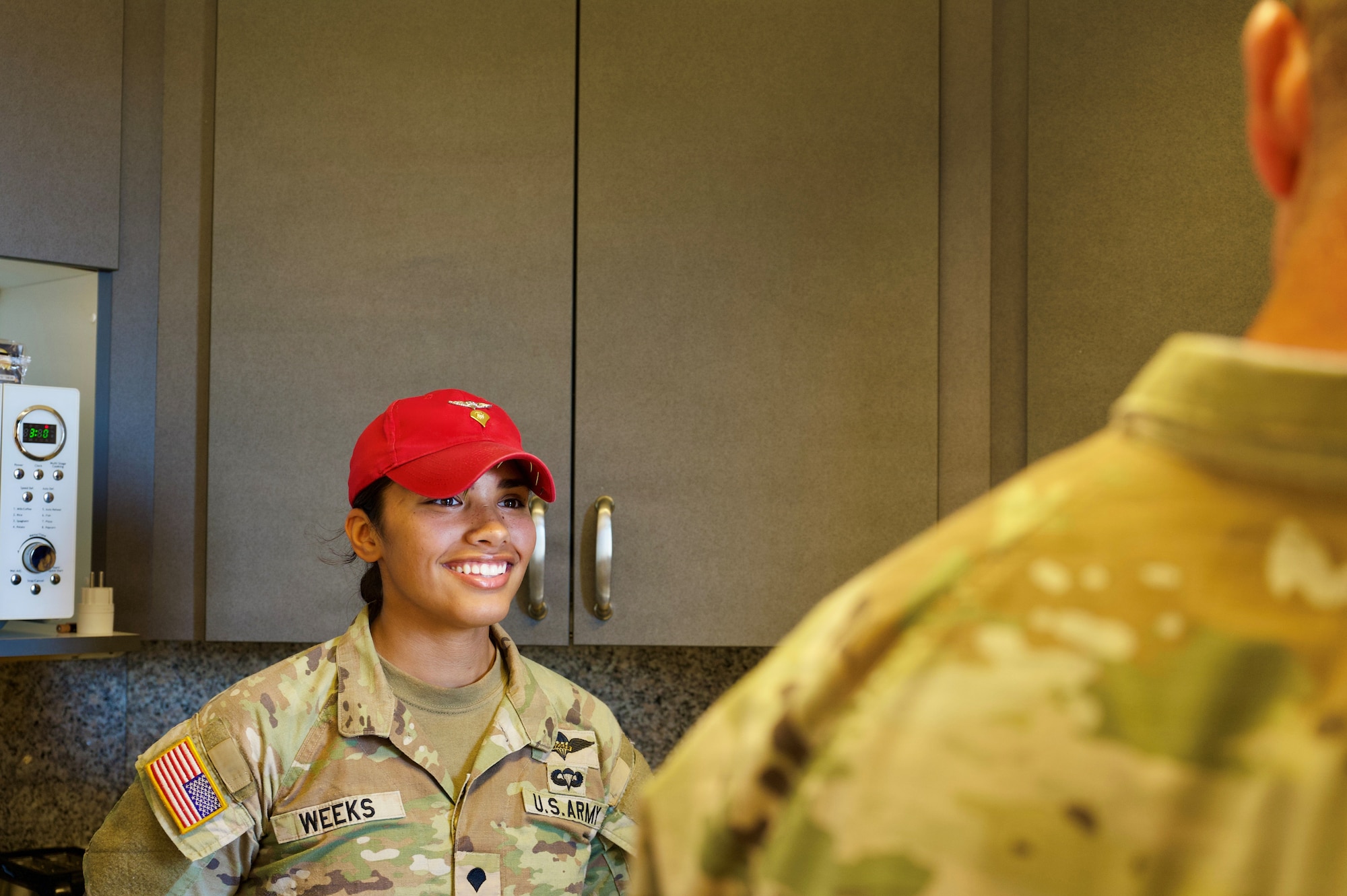 Female soldier in a red hat, smiles at another soldier.
