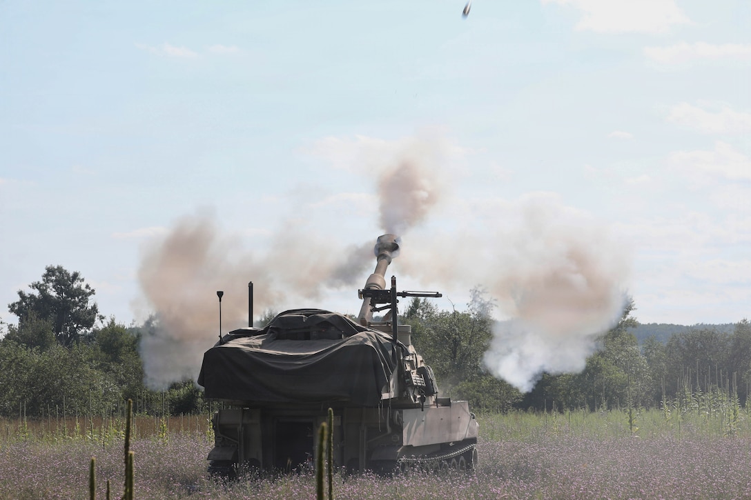 Soldiers fire artillery in a lavender field, leaving behind trails of smoke in blue sky.