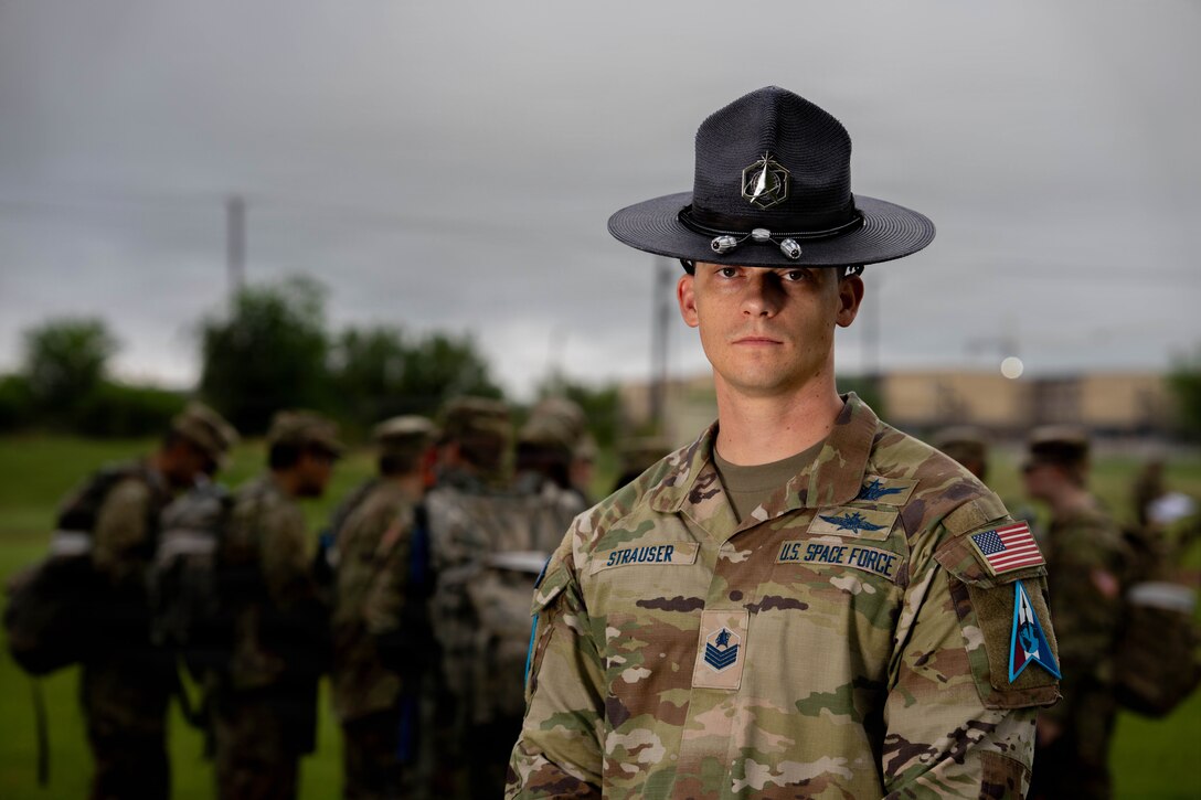 Military training instructor stands in uniform with cadets nearby outdoors