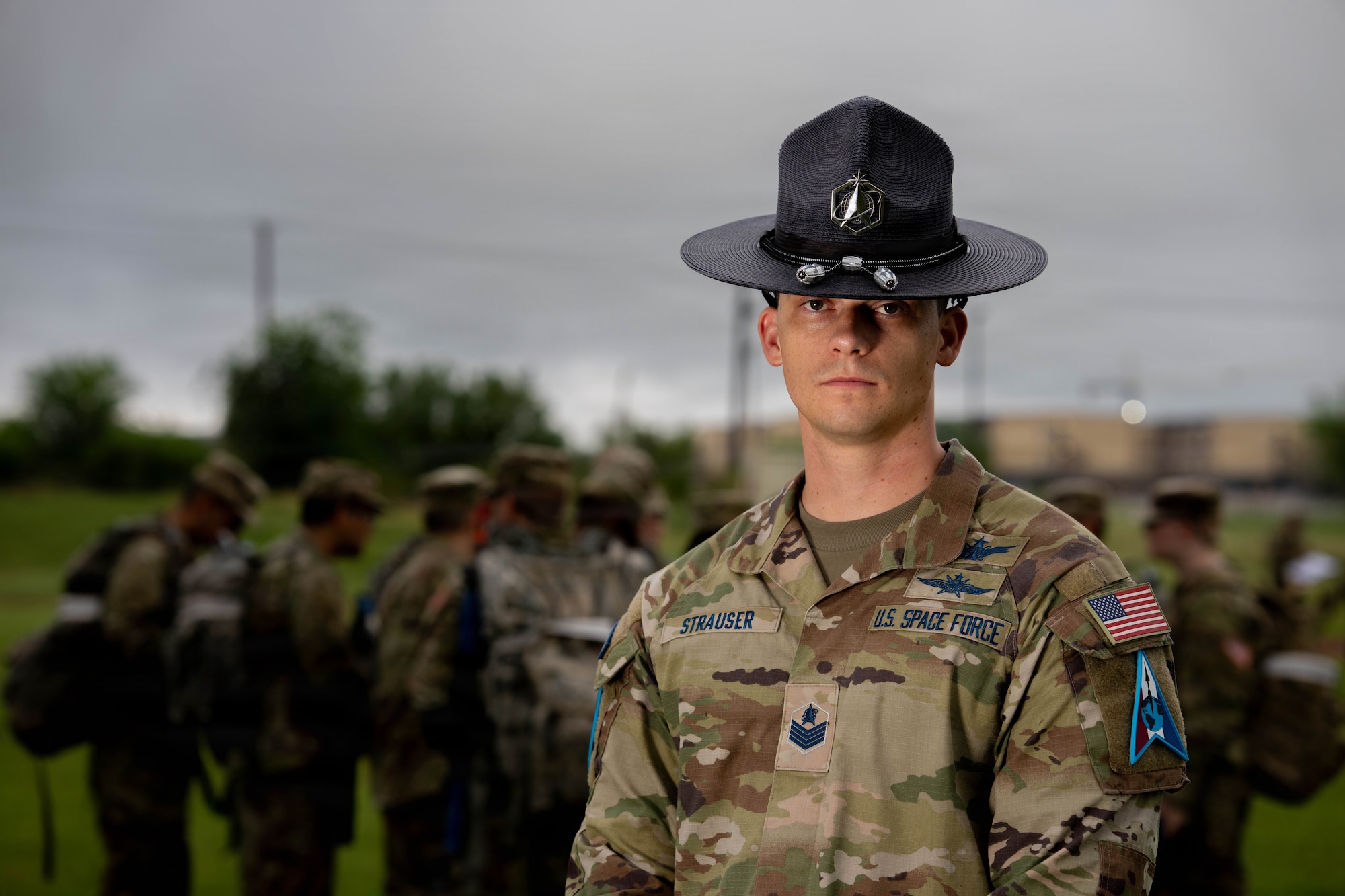 Military training instructor stands in uniform with cadets nearby outdoors