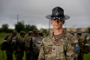 Military training instructor stands in uniform with cadets nearby outdoors