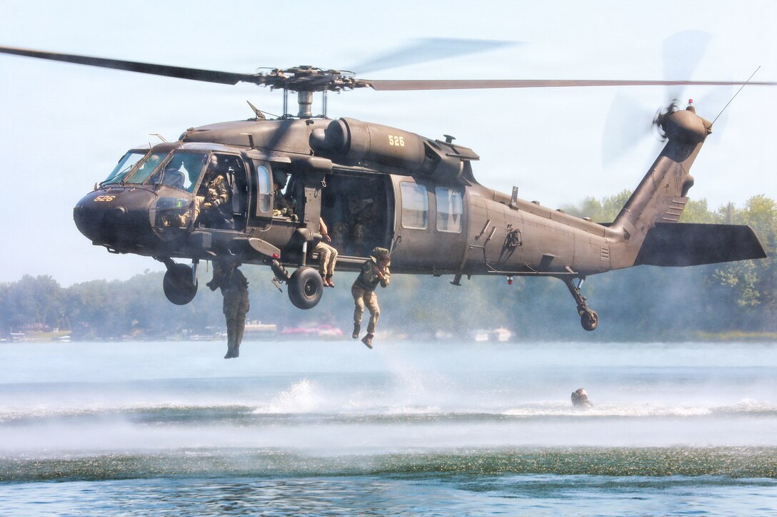 Service members jump from a hovering helicopter into a lake.