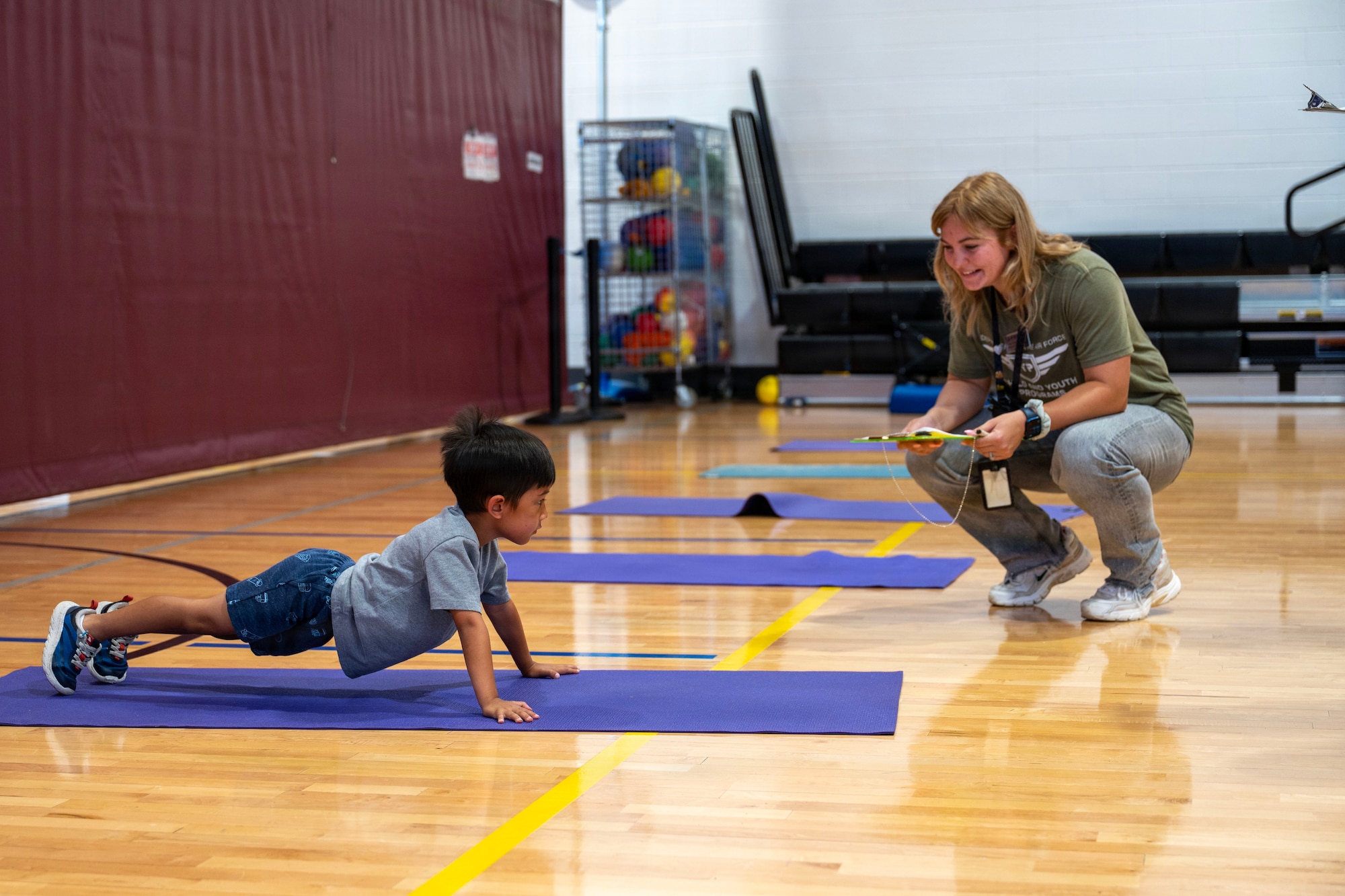 Student does push-ups on a basketball court while an instructor encourages him.