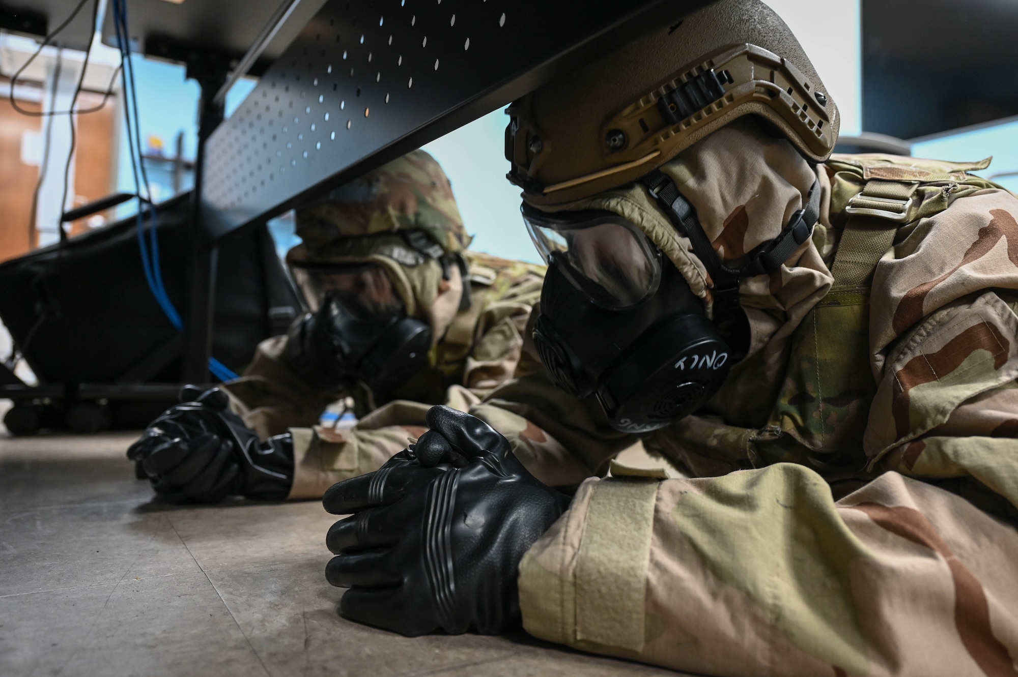Two Airmen lay in the ground under a table