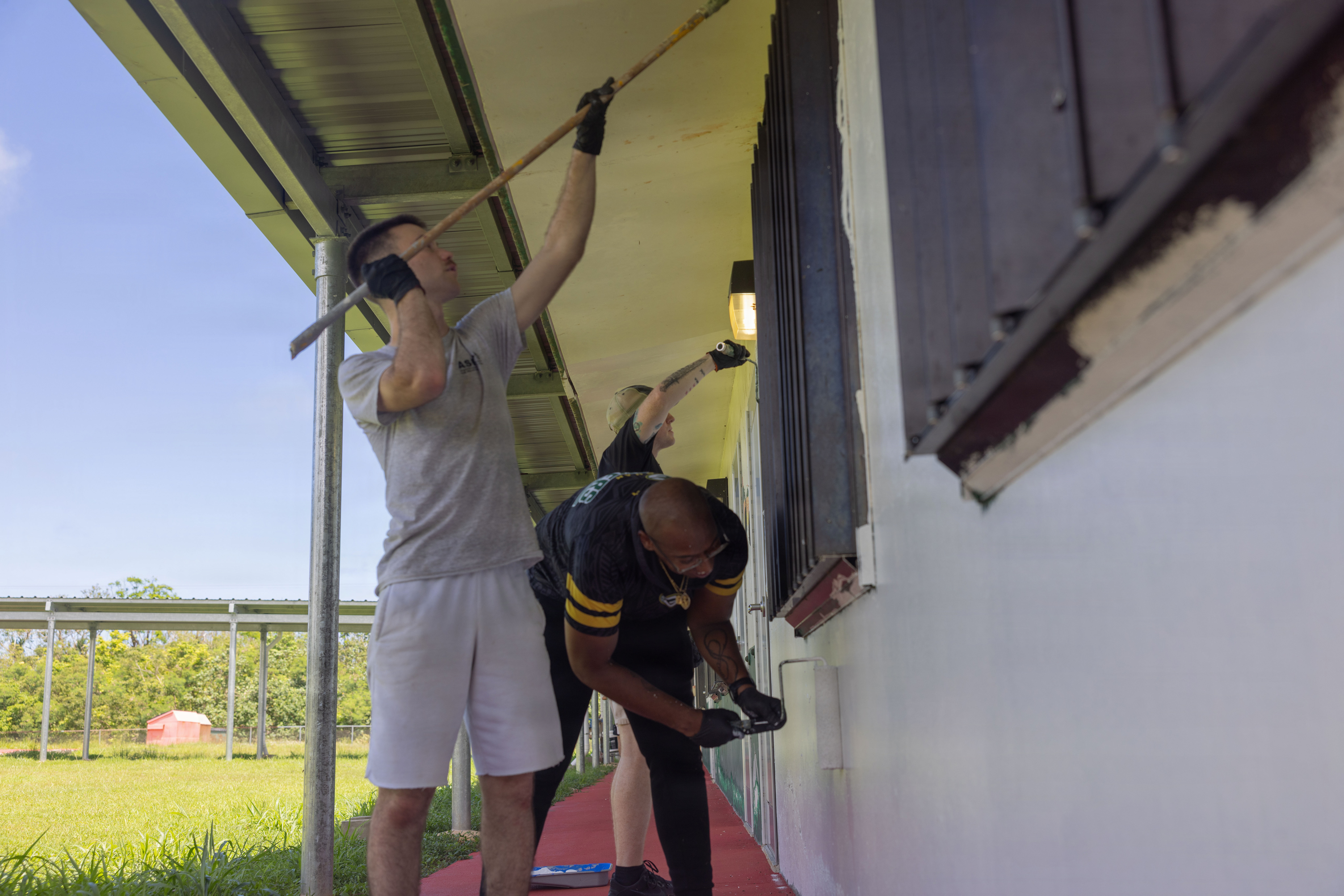 U.S Marine Corps Lance Cpl. Tanner Currin, combat graphics specialist, Gunnery Sgt. Marcellous Dixon, legal chief, and Maj. Mark Crum, communication strategy and operations director, all with Headquarters Company, Marine Corps Base Camp Blaz, paint a classroom building prior to the start of the school year at Finegayan Elementary in Dededo, Guam, July 31, 2026. Through the Joint Region Marianas "Sister School" program, Finegayan Elementary is MCB Camp Blaz's sister school, which the installation supports in academic, operational, and supplementary services. (U.S. Marine Corps photo by Sgt. Brayden Daniel)