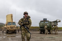 U.S Army Sgt. Blake Miller, 1st Squad leader assigned to 1st Battalion, 5th Infantry Regiment, 1st Mobile Brigade Combat Team (Air Assault), 11th Airborne Division pulls security in front of a AN/TP Q-53 Radar System and a High Mobility Artillery Rocket System assigned to the 17th Long Range Fires and Effects Brigade during Operation TUNDRA MERLIN near Nome, Alaska, Aug. 4, 2026. These Soldiers were deployed alongside the AN/TP Q-53 and HIMARS during TUNDRA MERLIN to demonstrate the joint forces' ability to rapidly deploy and seamlessly integrate combat equipment and personnel across the Arctic in defense of the Homeland and its approaches. (U.S. Air Force photo by Staff Sgt. Christopher Chen)