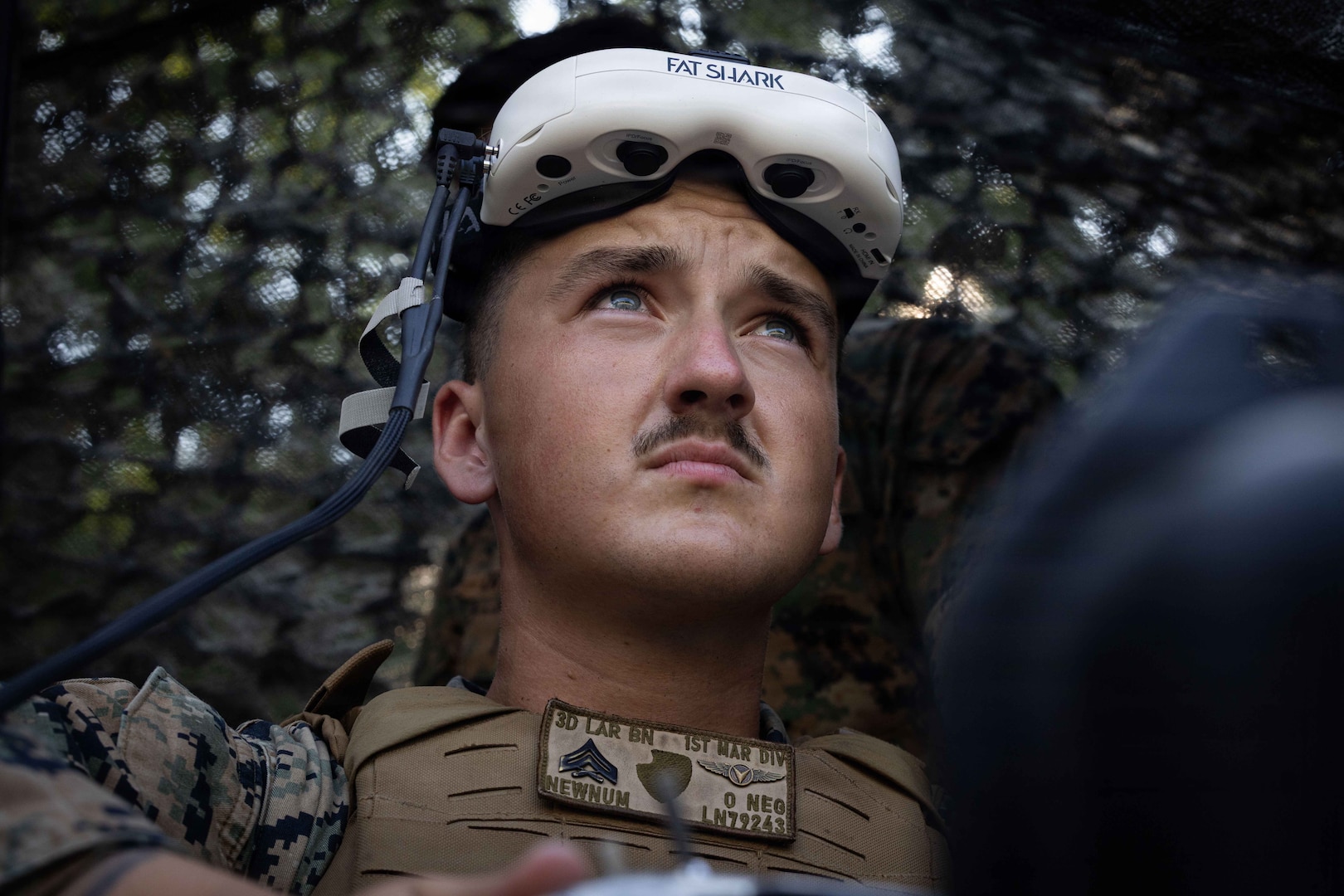 A man wearing a camouflage military uniform has a pair of military goggles on his face.