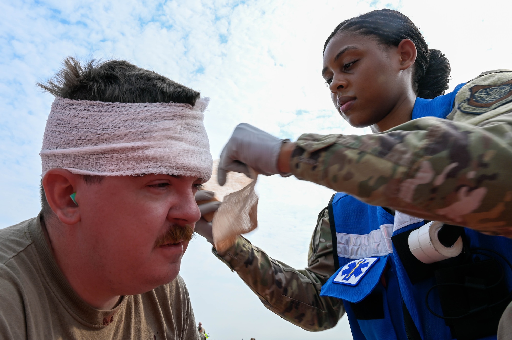 An Airman wraps a person's head with a bandage.