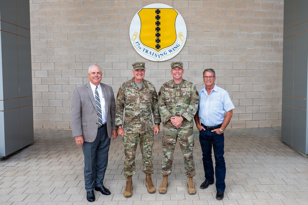 Four men stand smiling in front of a U.S. base emblem.