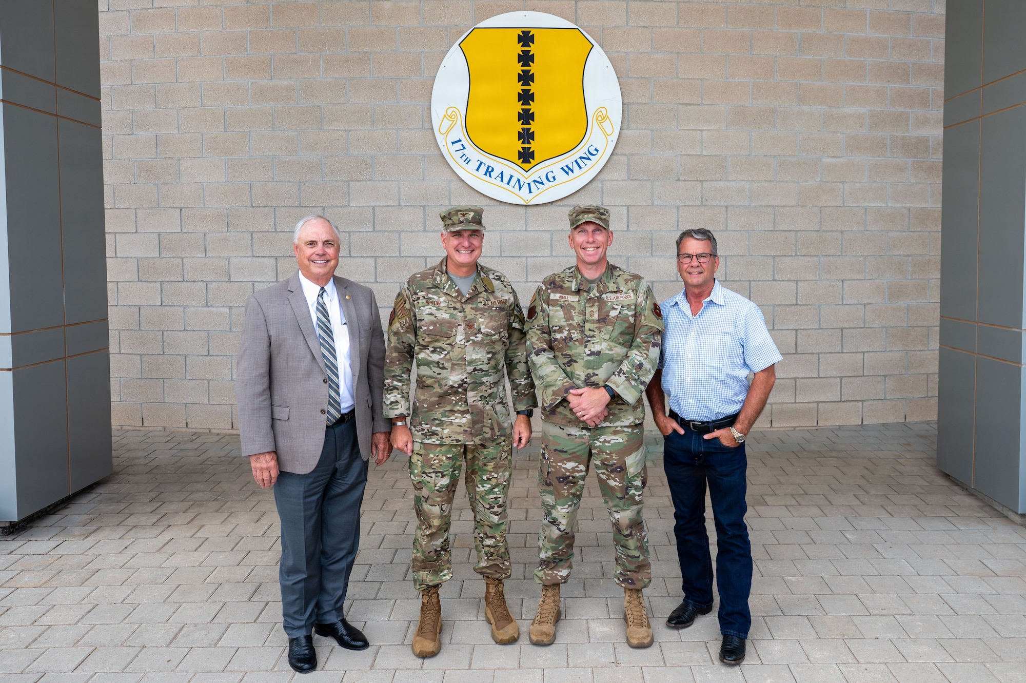 Four men stand smiling in front of a U.S. base emblem.