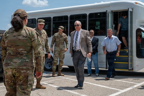 A group of people walk out of a white bus, greeted by U.S. Air Force members.