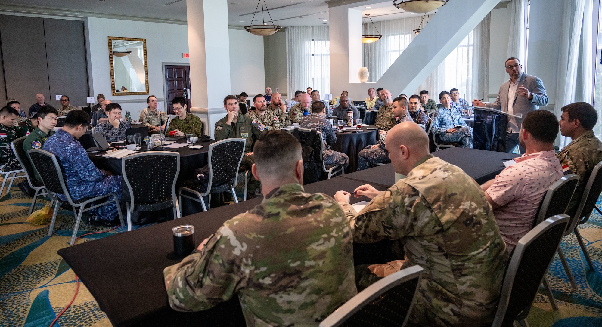 Photo of a person giving a speech to a crowd of military members from multiple nations.