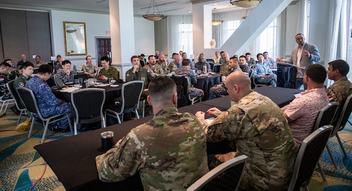 Photo of a person giving a speech to a crowd of military members from multiple nations.