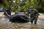 Members of Colombia's Military and the Policía Nacional de Panamá push a combat rubber raiding craft into the water