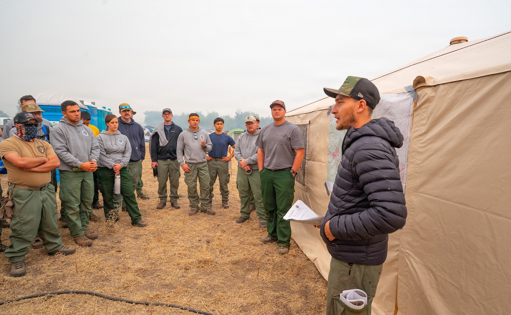 Giovanni Carranza, a crew boss with the California Smokejumpers, briefs Oregon Air National Guard hand crew members on their assignment for the day using a fire map at the Grasshopper Fire camp near Tygh Valley, Oregon, Aug. 9, 2026.
