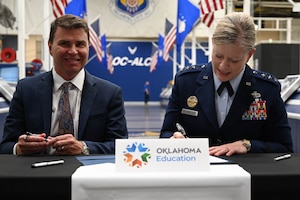 A man in a suit explains something while a person in a military uniform smiles and listens.