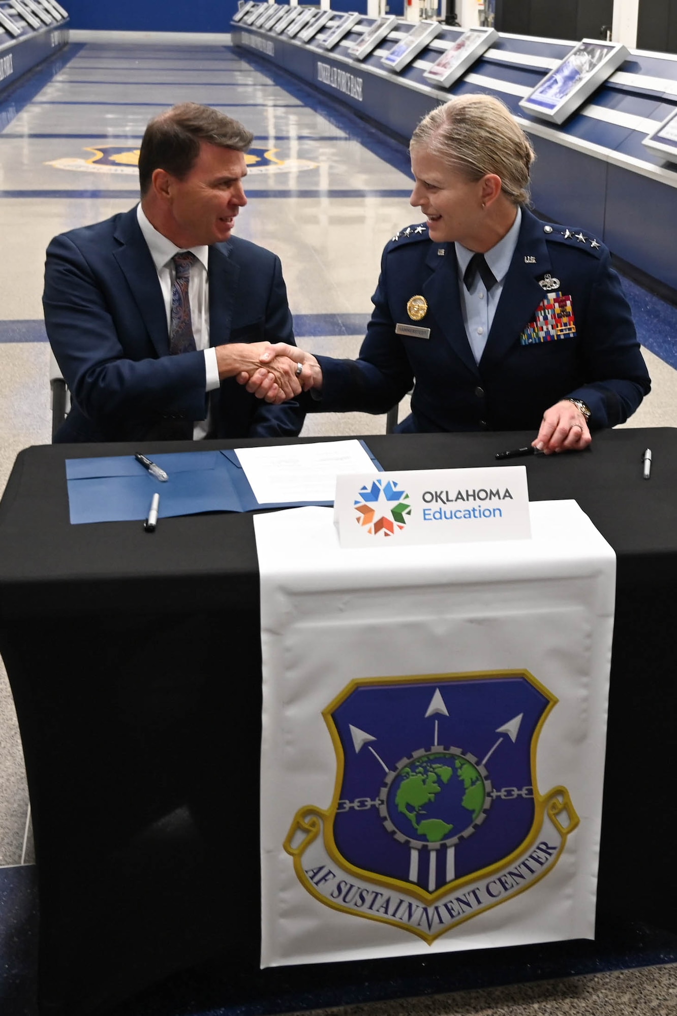 A man in a suit explains something while a person in a military uniform smiles and listens.