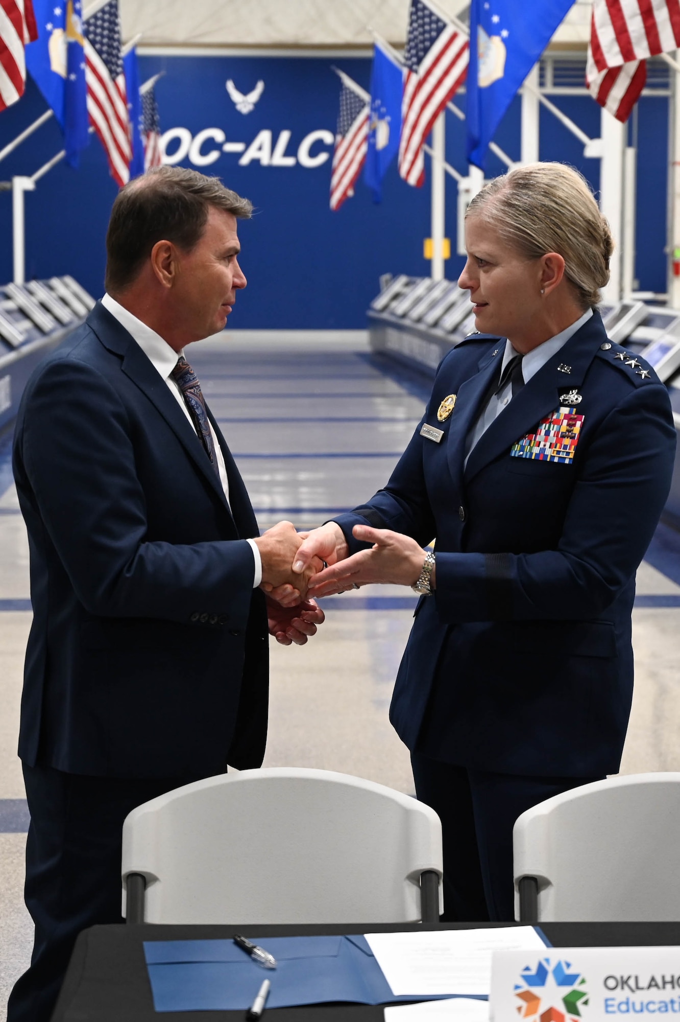 A man in a suit explains something while a person in a military uniform smiles and listens.