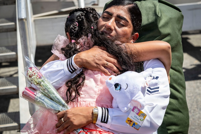 A woman in a white military uniform hugs a child while holding two red roses.