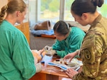 Nursing cadet draws blood from a simulated neo-natal patient as two others observe.