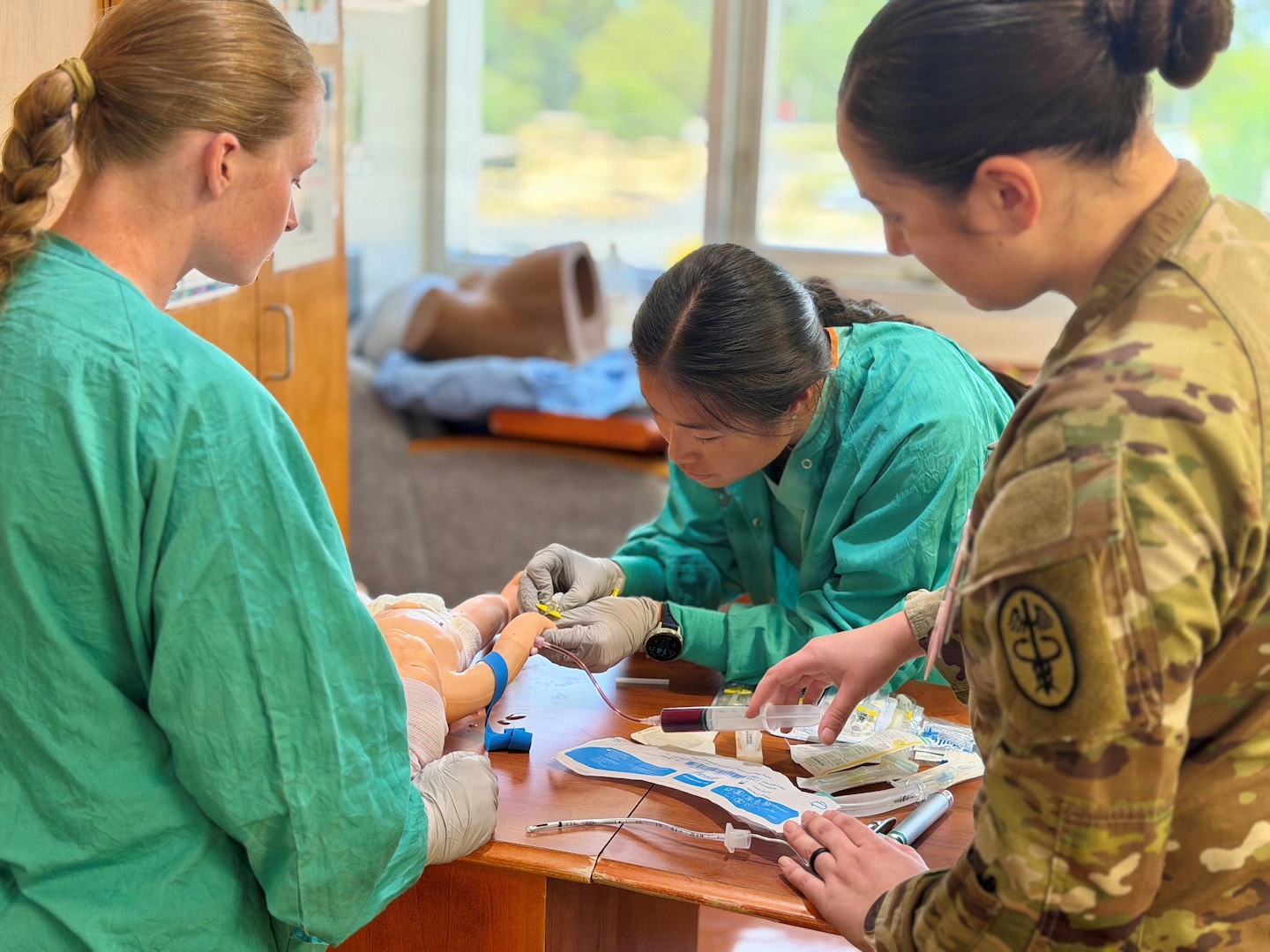 Nursing cadet draws blood from a simulated neo-natal patient as two others observe.
