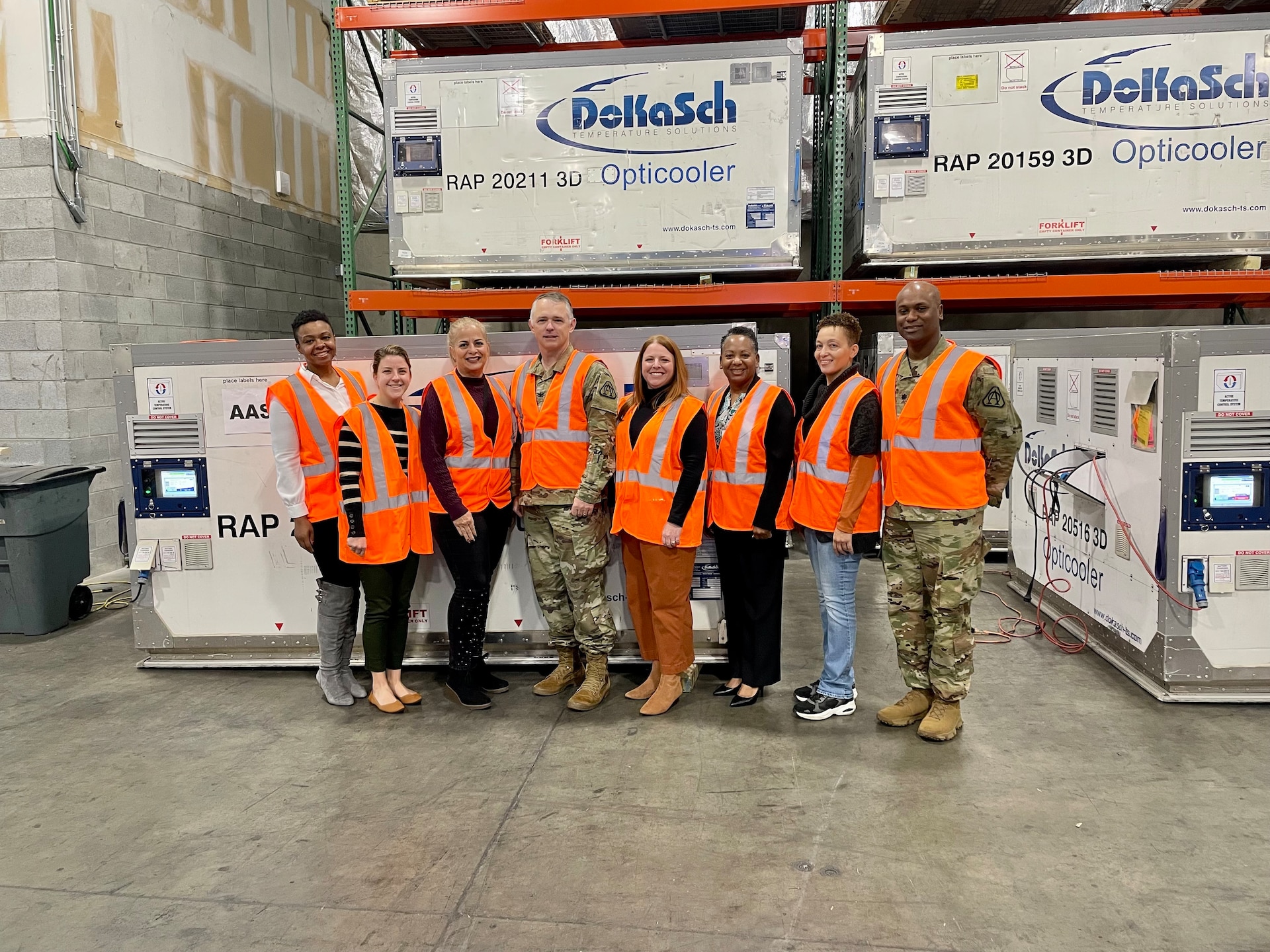 Eight team members in orange vests in a warehouse.