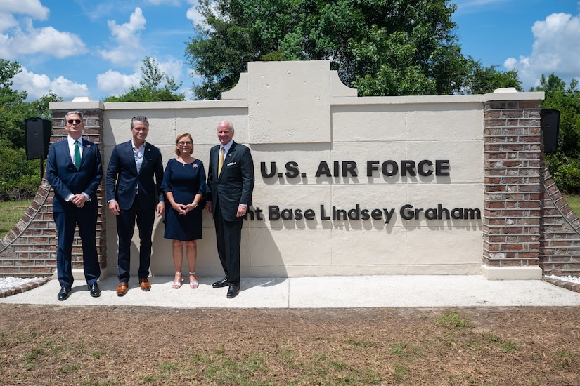 Four people in business attire stand in front of a sign that reads, "U.S. Air Force Joint Base Lindsey Graham."