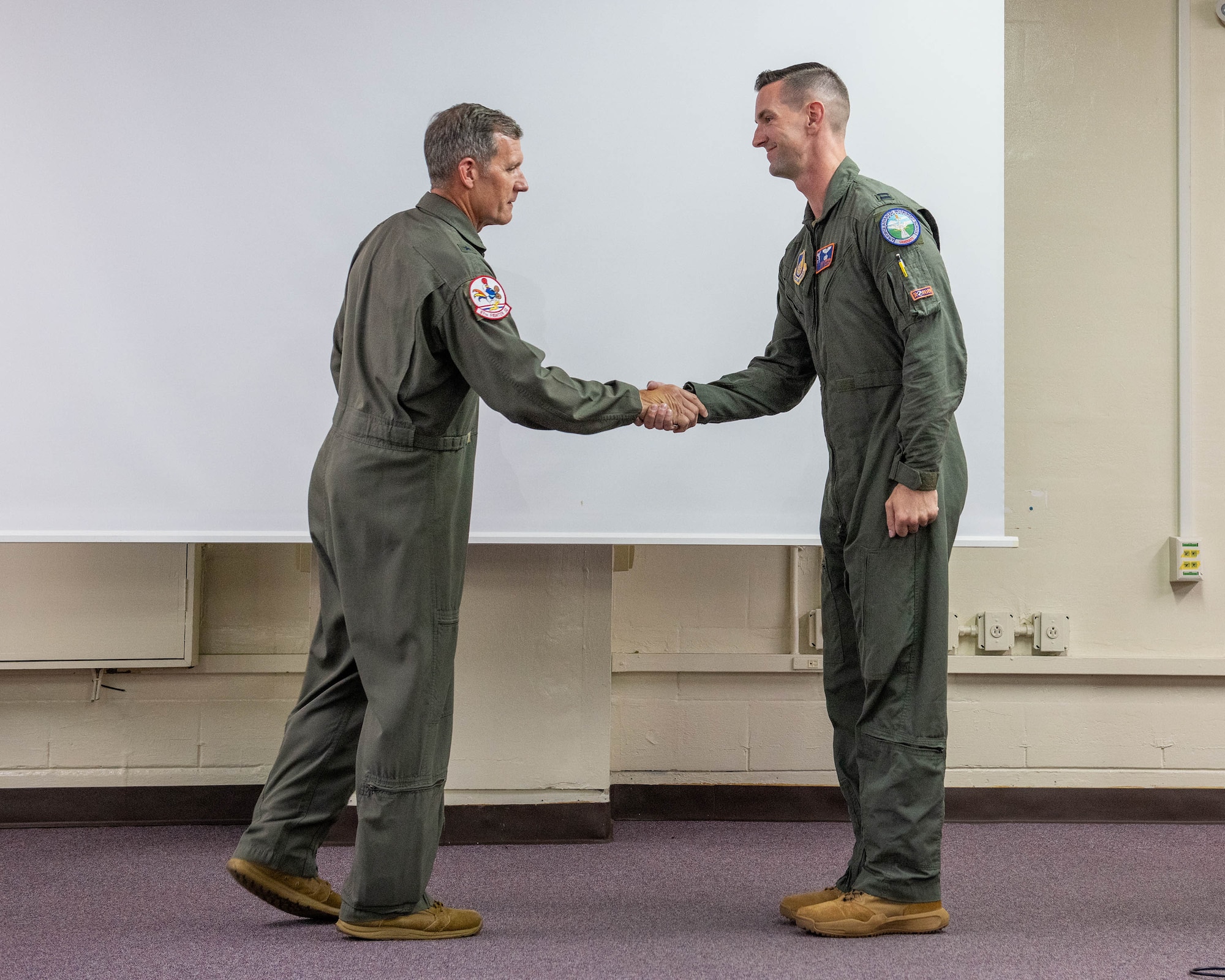 U.S. Air Force Capt. Zach Siefken, right, 961st Airborne Air Control Squadron E-3 Century pilot gets coined by Brig. Gen. John Gallemore, 18th Wing commander at Kadena Air Base, Japan, July. 23, 2026. The recognition honored their quick actions during a medical emergency in Chatan Town, where they assisted fellow neighbors in providing lifesaving aid to a U.S. service member. (U.S. Air Force photo by Naoto Anazawa)