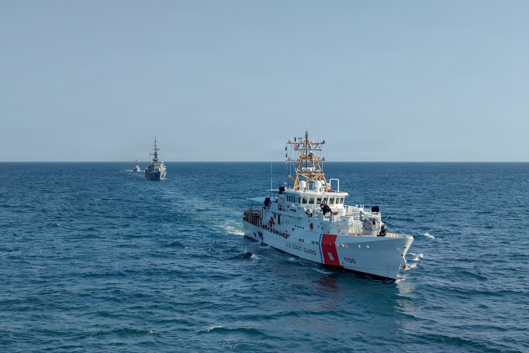 Three ships sail in formation in a body of water during the day.