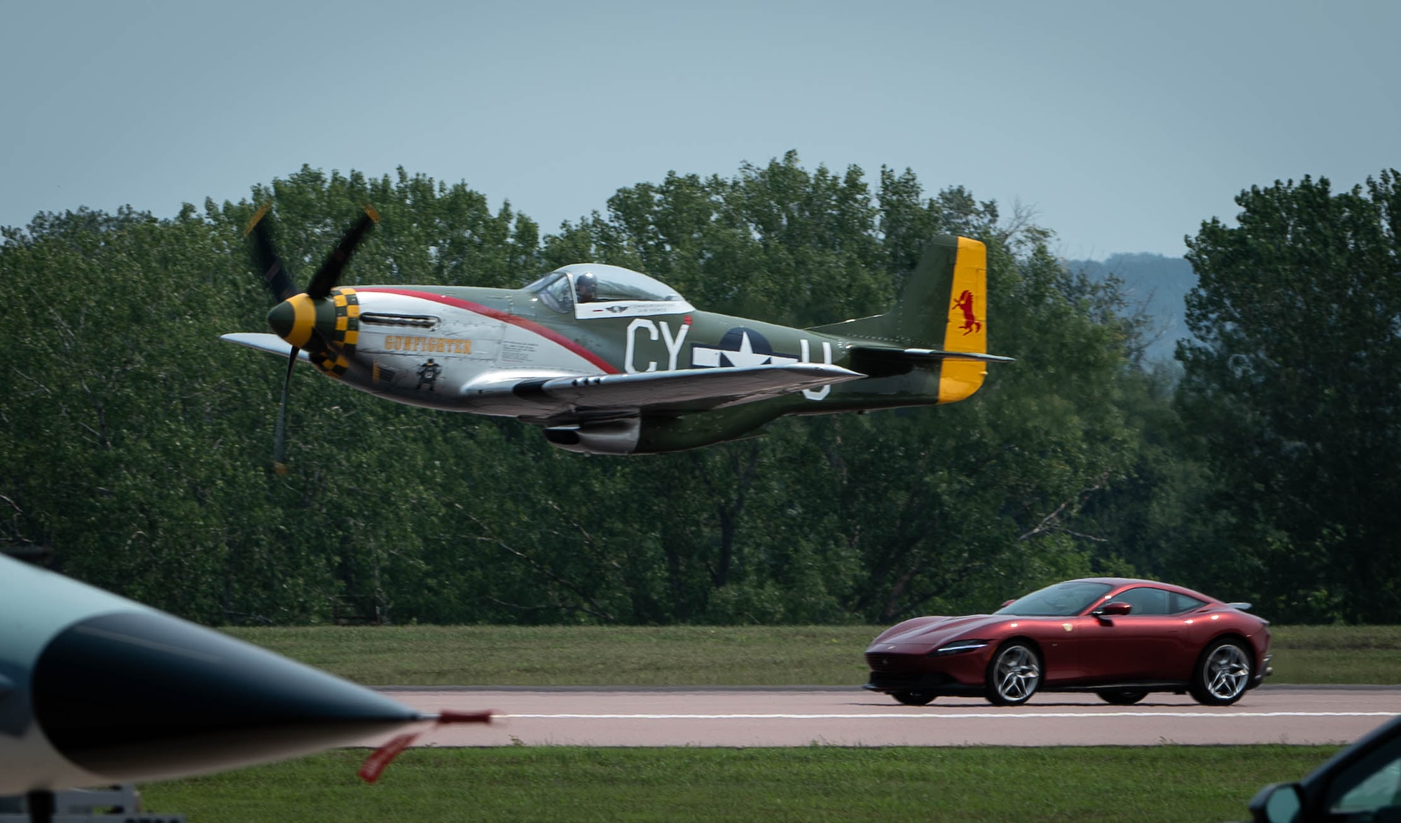 A T-28 Trojan races a Porsche 911 GT3 during the 2026 Defenders of Freedom Air & Space Show at Offutt Air Force Base, Nebraska, Aug. 9, 2026. The event served as a platform to celebrate Offutt AFB's military heritage, honoring the unique civilian-military bond with the Greater Omaha community that has supported the nation's defense for generations. (U.S. Air Force photo by Daniel Martinez)