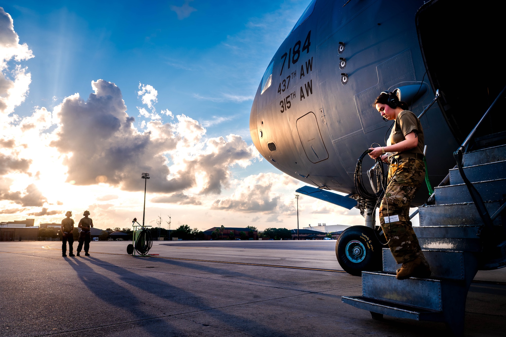 A photo of a U.S. Air Force Airman walking down a C-17 Globemaster III ramp with two more Airmen standing in the background.