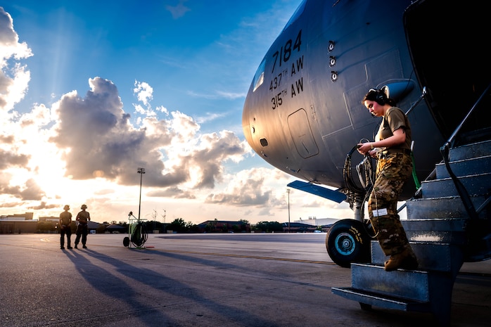 A photo of a U.S. Air Force Airman walking down a C-17 Globemaster III ramp with two more Airmen standing in the background.
