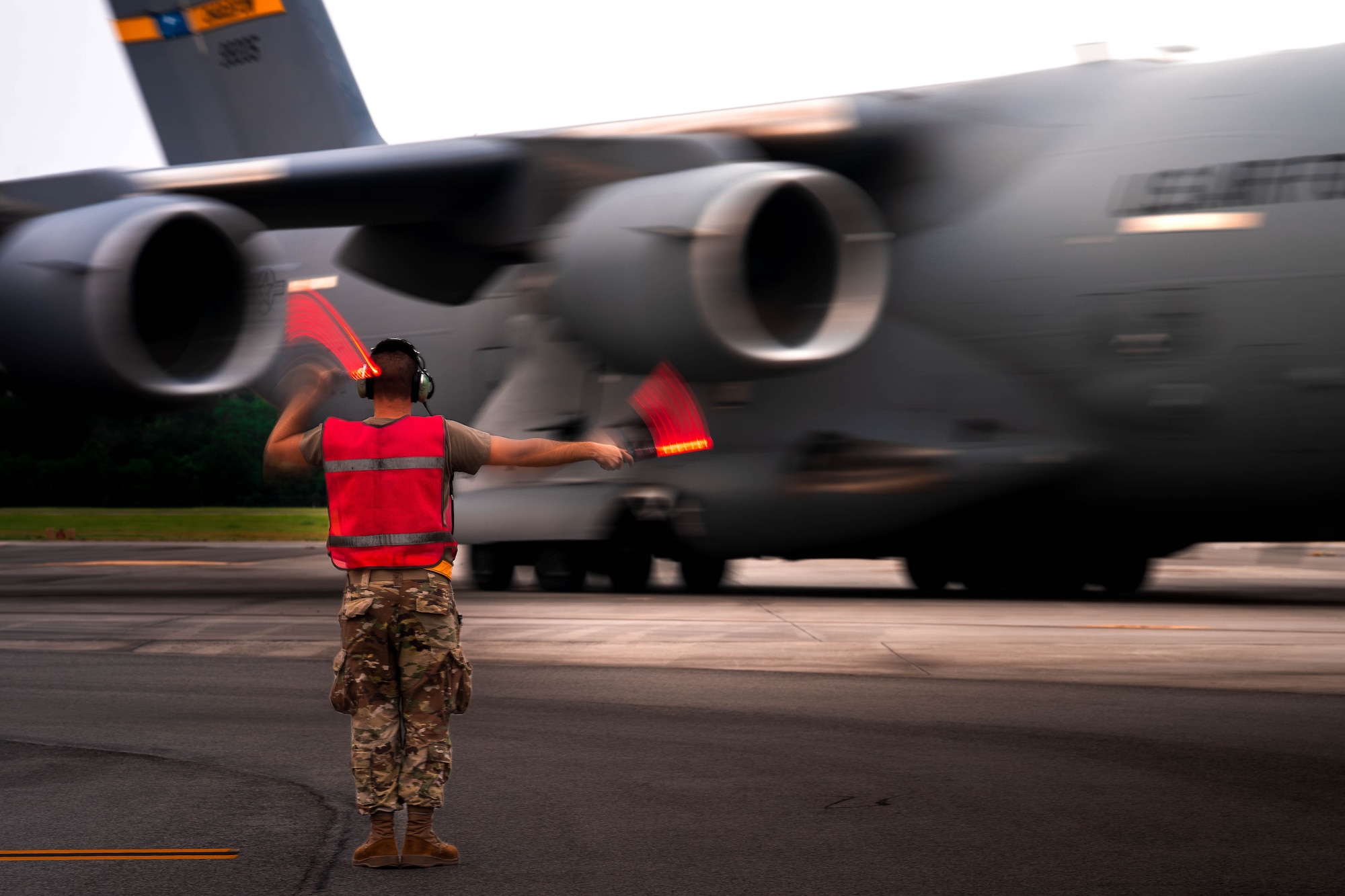 A photo of an Airman marshaling a C-17 Globemaster III across a flightline.