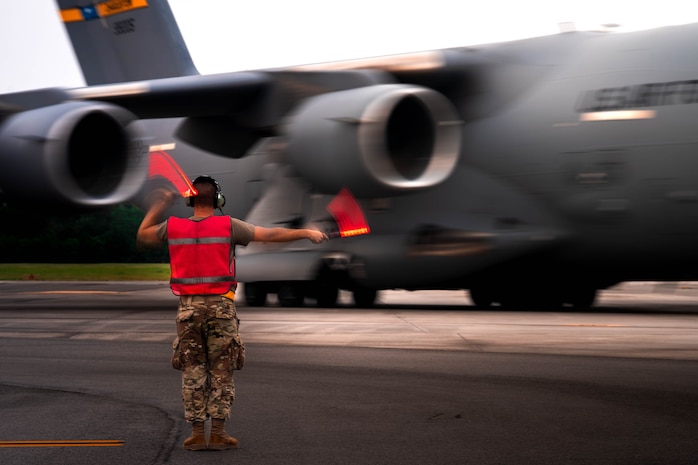 A photo of an Airman marshaling a C-17 Globemaster III across a flightline.