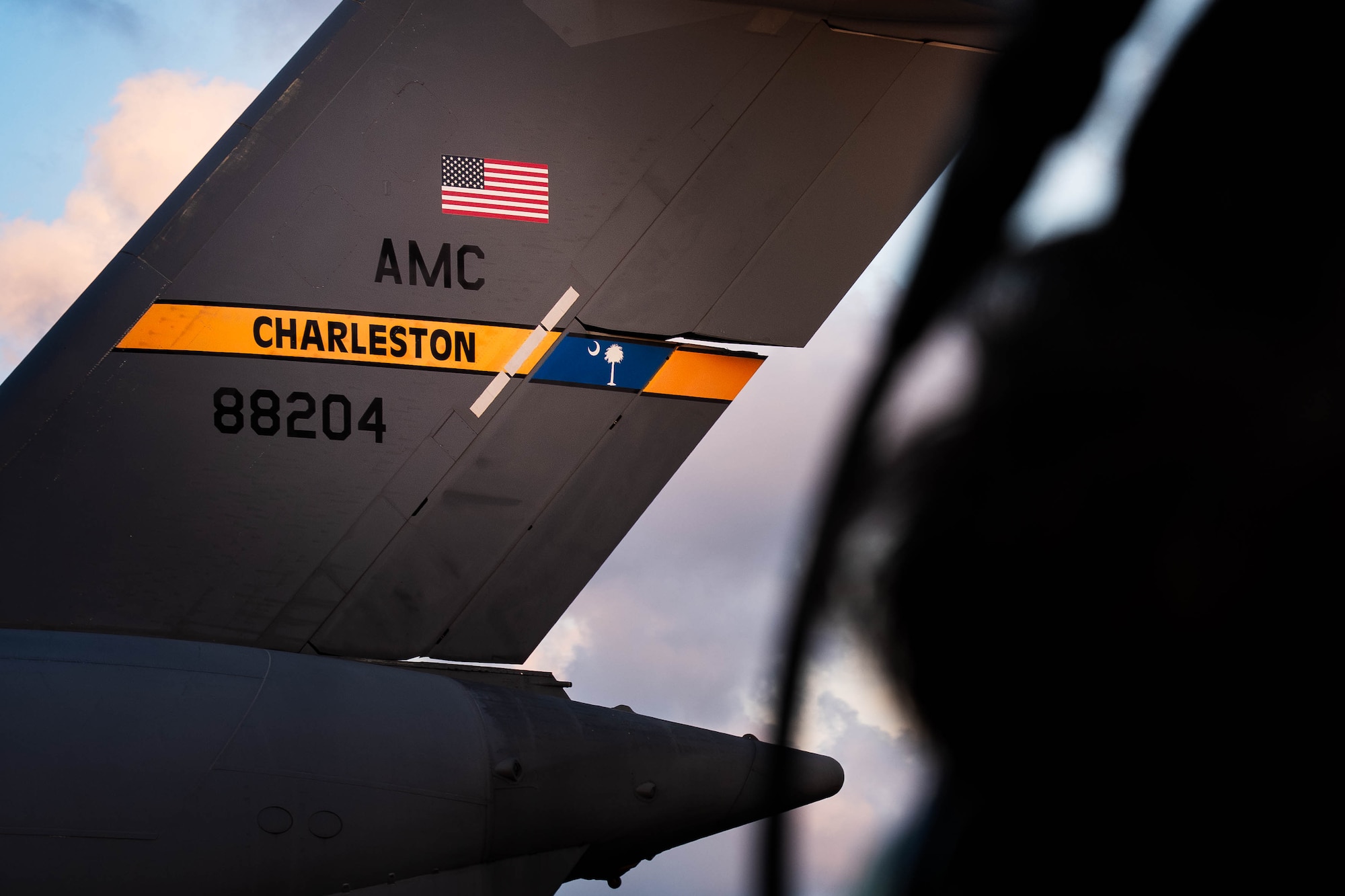 A photo of a C-17 Globemaster III driving across the flightline. There's a silhouette of an Airman in the foreground.