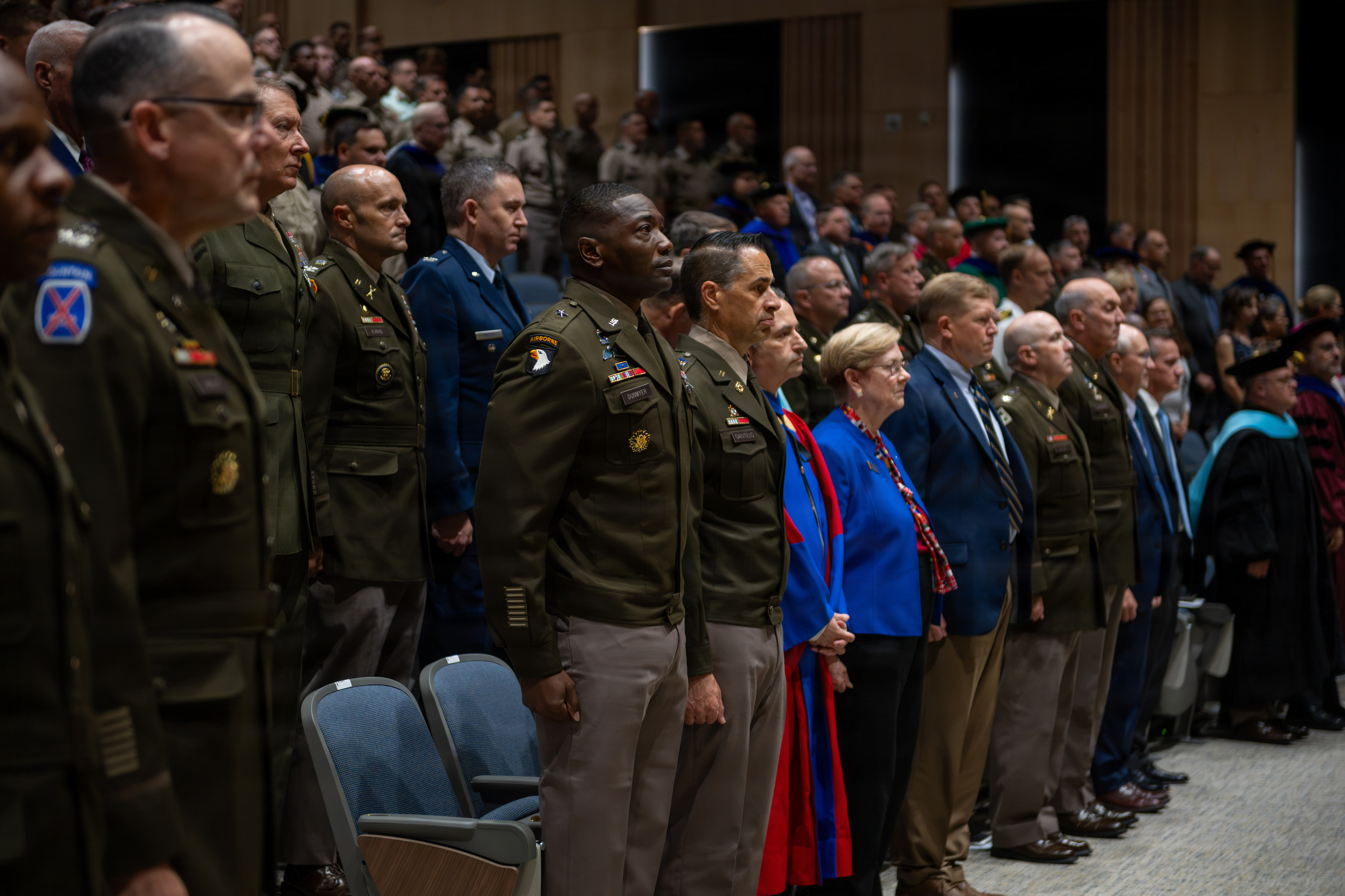 A large group of joint military officers in various service uniforms and civilians in professional attire stand inside Bliss Auditorium at Carlisle Barracks during the U.S. Army War College Class of 2027 convocation ceremony.