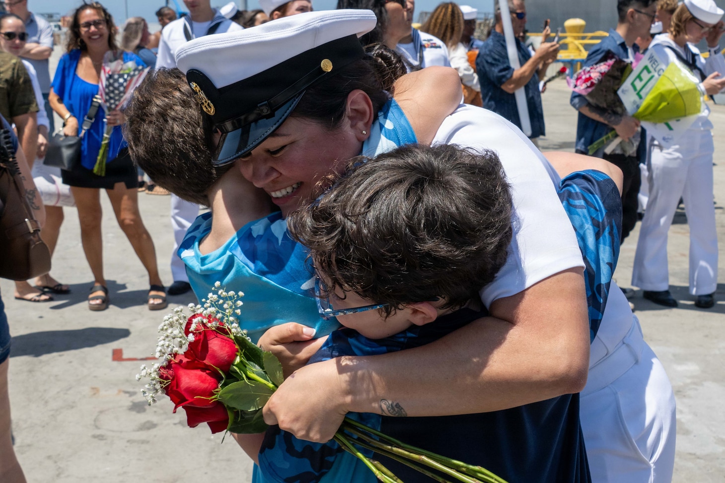 A U.S. Navy Sailor in dress whites embraces family members on the pier during the homecoming of USS Pinckney (DDG 91).