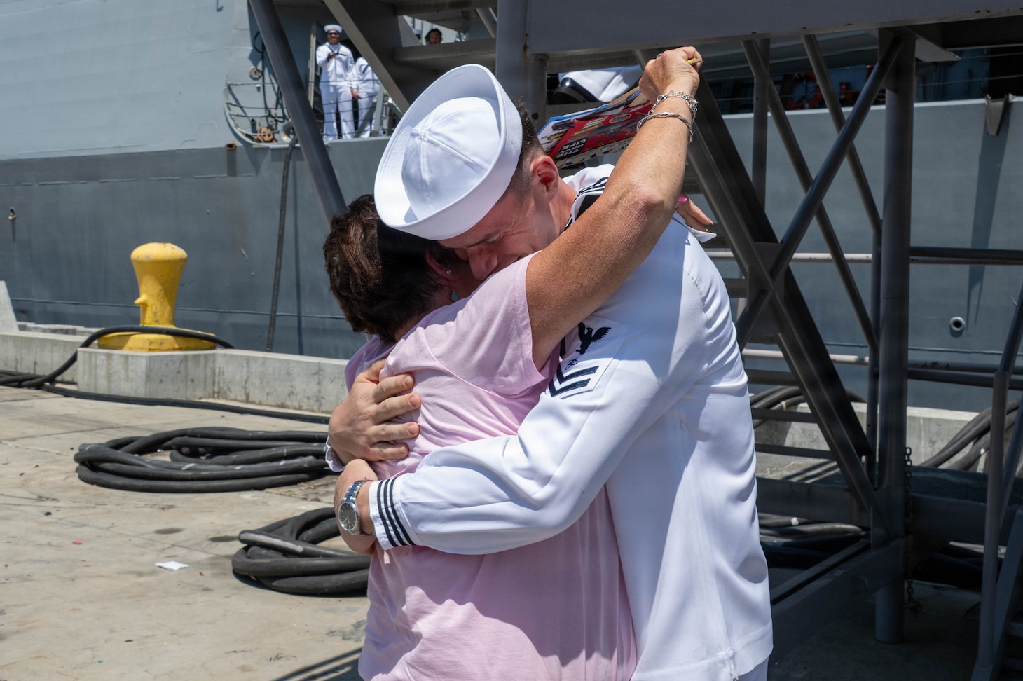 A U.S. Navy Sailor in dress whites embraces a loved one on a pier at the homecoming of USS Pinckney (DDG 91).