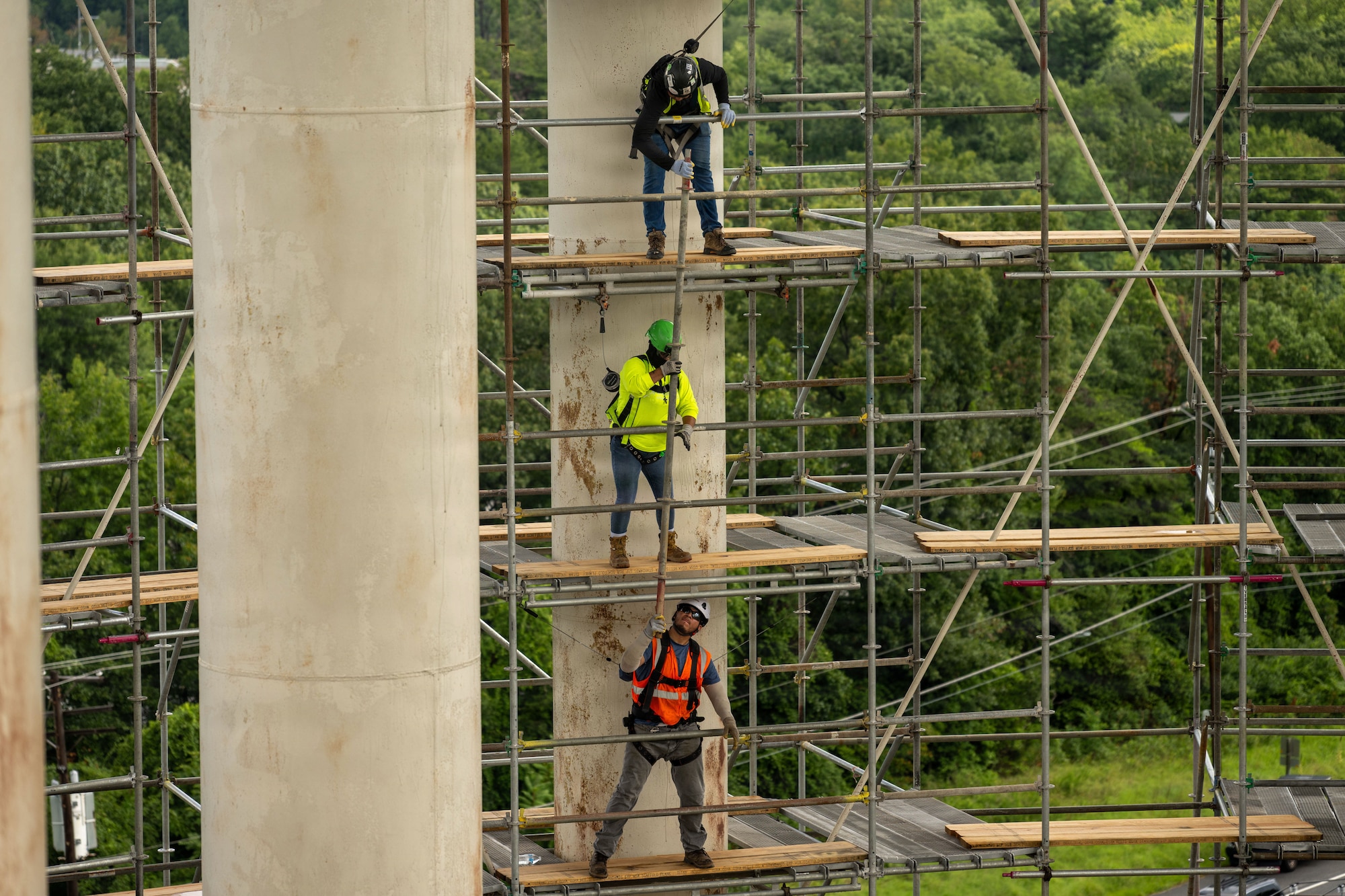 Three men stand one above another on scaffolding.