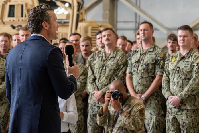 A man speaks towards a group of people in an overhead building.